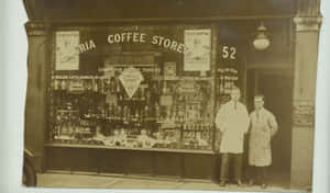 兩名身穿白袍的男子站在一間有玻璃陳列櫃的復古咖啡店外。 — 70年代動圖 壁紙