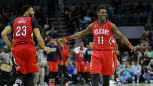 兩名身穿紅色Pelicans球衣的籃球運動員在燈光明亮的球場上張開雙臂，笑容燦爛地慶祝一次進攻。 — 紐奧良鵜鶘 壁紙