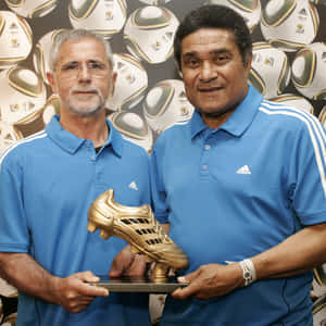 兩名身穿藍色襯衫的男子手持金色足球靴獎盃。 — FIFA 世界盃 壁紙