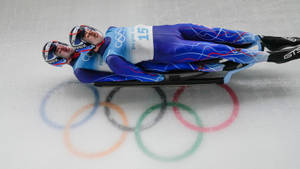 兩名雪橇運動員在冰上競賽，下方有彩繪的奧運五環。 — 極限運動 壁紙