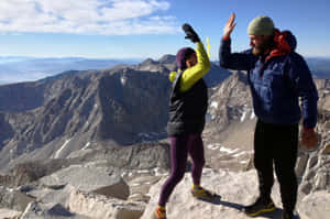 兩人在山頂上擊掌，俯瞰廣闊的岩石景觀。 — 登山 壁紙