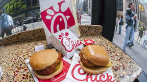 兩塊Chick-fil-A雞肉三明治放在斑點桌上，窗外是城市街景。 — 海鮮 壁紙