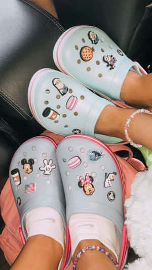 兩個人穿著裝飾過的Crocs鞋，帶有迪士尼和小小兵吊飾，坐在沙發上。 — Crocs 壁紙