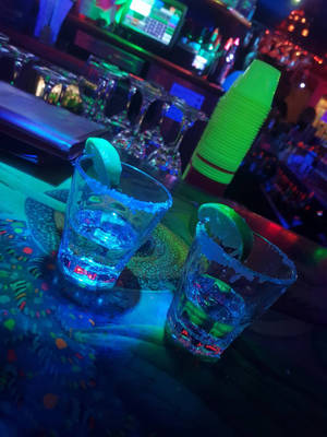 兩杯藍色發光瑪格麗特酒，配以萊姆裝飾，在霓虹酒吧上。 — 3:4 壁紙