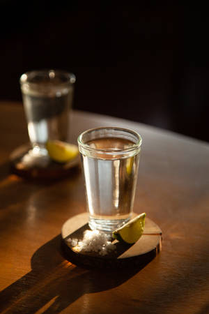 兩杯龍舌蘭酒配上鹽和萊姆，放在木杯墊上，置於深色木桌上。 — 小米平板 7S Pro 12.5 壁紙