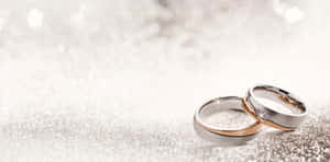 兩枚結婚戒指，一枚玫瑰金一枚銀色，在閃爍的銀色表面上。 — 結婚戒指 壁紙