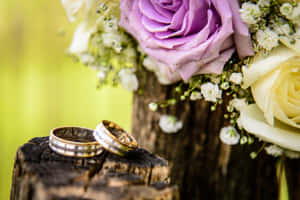 兩枚刻有圖案的結婚戒指在樹樁上，伴隨著一束花。 — 結婚戒指 壁紙