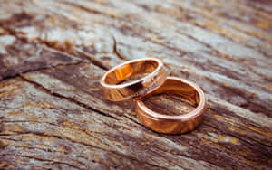 兩枚玫瑰金結婚戒指鑲有鑽石，放在質樸的木頭上。 — 結婚戒指 壁紙