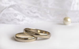 兩枚銀色結婚戒指，背景有珍珠和蕾絲。