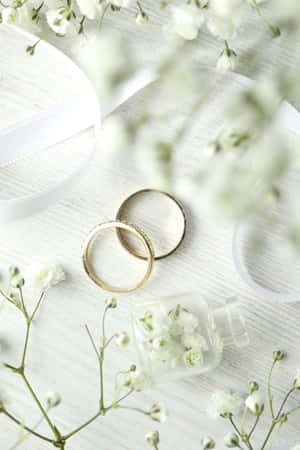 白色木質表面上的兩枚金色結婚戒指，搭配滿天星和絲帶。 — Oppo Pad 壁紙