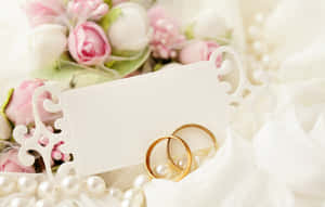 金色結婚戒指放在珍珠上，配以花朵和卡片，適合新娘主題。 — 結婚戒指 壁紙