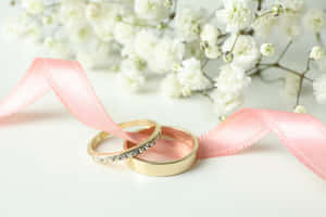 兩枚結婚戒指配以粉紅色絲帶和白色花朵，適合浪漫慶祝。 — 婚禮 壁紙