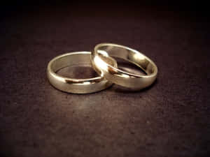 兩枚銀色結婚戒指在深色紋理表面上交織。 — 結婚戒指 壁紙