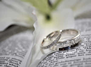 兩枚結婚戒指放在打開的書上，旁邊有一朵白百合。 — 結婚戒指 壁紙
