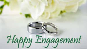 兩枚銀色訂婚戒指，配白玫瑰和綠色 Happy Engagement 文字。 — 情侶 壁紙