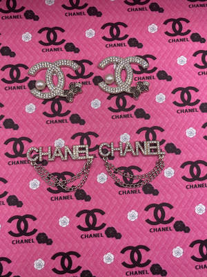 兩枚 Chanel 胸針，飾有珍珠和鏈條，放在品牌粉紅色布料上。 — 粉嫩粉彩美學 壁紙