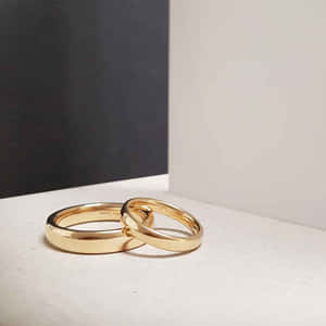 兩枚金色結婚戒指交織在白色表面上，黑白背景。 — 婚禮 壁紙
