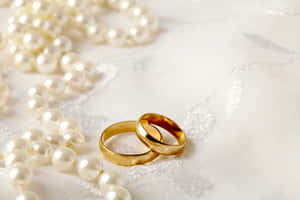 白色蕾絲布料上的兩枚黃金結婚戒指和一條珍珠項鍊。 — 結婚戒指 壁紙