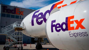 兩架 FedEx 貨機停泊在機場閘口，後面是 FedEx 大樓。 — 聯邦快遞 壁紙