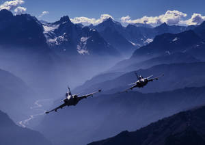 兩架戰鬥機在晴朗的藍天中飛越白雪覆蓋的山脈。 — 空軍 壁紙