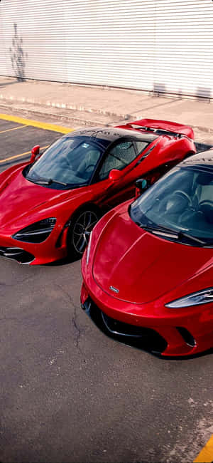 日落時分，兩輛紅色McLaren超級跑車停放在城市停車場。 — Redmi Note 14 Pro 壁紙