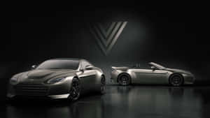 兩輛消光灰色 Aston Martin 跑車在黑暗的攝影棚中，配有聚光燈和標誌。 — 奧斯頓馬丁 壁紙