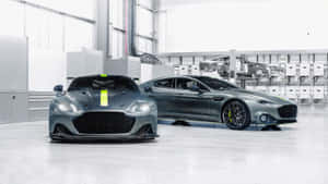 工廠內兩輛帶有黃色點綴的灰色 Aston Martin 跑車。 — 奧斯頓馬丁 壁紙