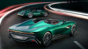 兩輛綠色 Aston Martin 跑車在賽道上競速，帶有光軌。 — 阿斯頓維拉 壁紙