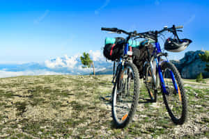 兩輛登山自行車停在高高的岩石山脊上，下方有雲，遠處有山。 — 登山車 壁紙