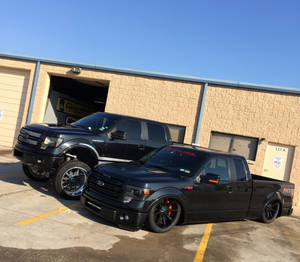 兩輛黑色訂製福特F-150皮卡車停放在車庫前。 — 墜落卡車 壁紙