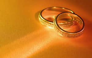 兩隻金色結婚戒指，邊緣帶有紋理，在溫暖光線下閃耀。 — 珠寶 壁紙