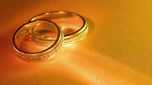 兩隻帶有紋理帶的金色結婚戒指，在金色皮革背景上。 — 結婚戒指 壁紙