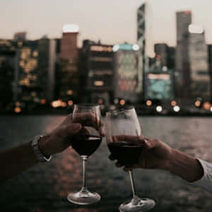 兩人在黃昏時分以城市天際線為背景碰杯。 — 葡萄酒 壁紙