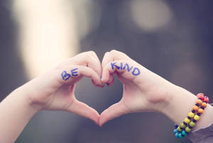 兩隻手形成心形，手掌上寫有「BE KIND」，一隻手腕上戴著彩色手鐲。 — 愛心 壁紙