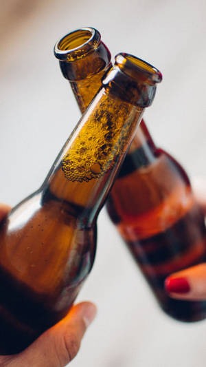 兩隻手碰撞啤酒瓶，進行慶祝乾杯。 — 啤酒 壁紙