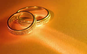 兩隻帶有紋理帶的金色結婚戒指放在溫暖的金色表面上。 — 16:10 壁紙