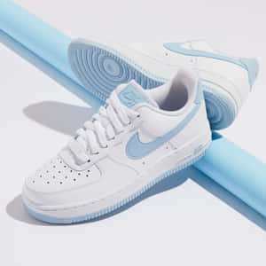白色Nike Air Force 1運動鞋，帶有淺藍色細節，置於藍色圓柱體和白色表面上。 — 海軍藍 壁紙