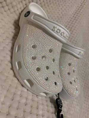 白色Crocs鞋覆蓋水鑽，放在白色有紋理地毯上。 — Crocs 壁紙