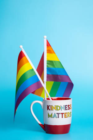 一個寫有 kindness matters 的杯子在藍色背景下舉著兩面彩虹驕傲旗。 — 彩虹旗 壁紙