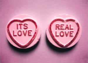 兩顆粉紅色心形糖果，帶有紅色閃粉文字，上面寫著「ITS LOVE」和「REAL LOVE」。 — 愛就是愛 壁紙