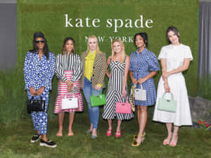 六位穿著時尚服裝和手提包的女性在草地上參加 Kate Spade 活動時擺姿勢。 — Kate spade 壁紙