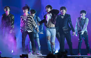 K-pop 組合在煙霧和動態姿勢的燈光舞台上表演。 — MacBook Pro M2 壁紙