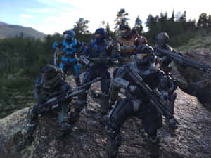 六個Halo Spartan動作人偶在森林覆蓋的山景中，於岩石山坡上擺出姿勢。