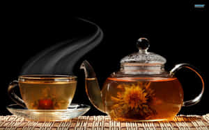 玻璃茶壺和杯子，裝有冒煙的花草茶和盛開的花朵，放在編織墊上。 — 茶 壁紙