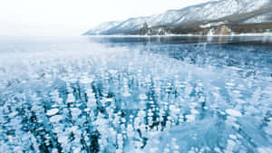 冰凍的湖面，帶有冰泡，映照著積雪的山峰。 — 湖泊 壁紙