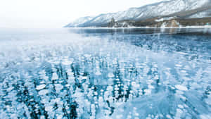冰封湖面帶有冰泡，映照積雪覆蓋的山峰 — 冬季風景 壁紙