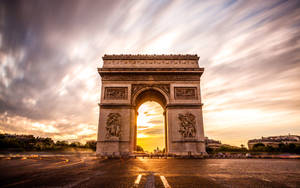 凱旋門被金色日落光芒照亮，天空中有條紋雲彩。 — 法國 壁紙