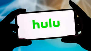 兩隻手拿著一部顯示 Hulu 標誌的電話。 — 葫蘆 壁紙
