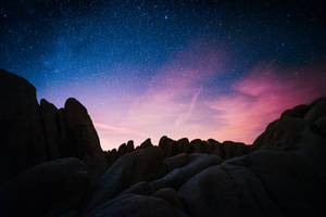 在帶有粉紅色和紫色色調的星空暮色下的黑暗岩石。 — 夜晚 壁紙