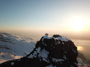 日出時白雪覆蓋的山頂上的登山者，俯瞰峽灣 — 寒冷 壁紙